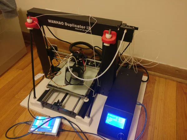 A 3d printer in a state of partial disassembly, with additional cables and screen attached to it.