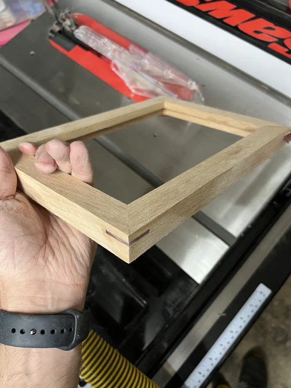 Hand holding a picture frame with edge having a spline glued in using contrasting wood